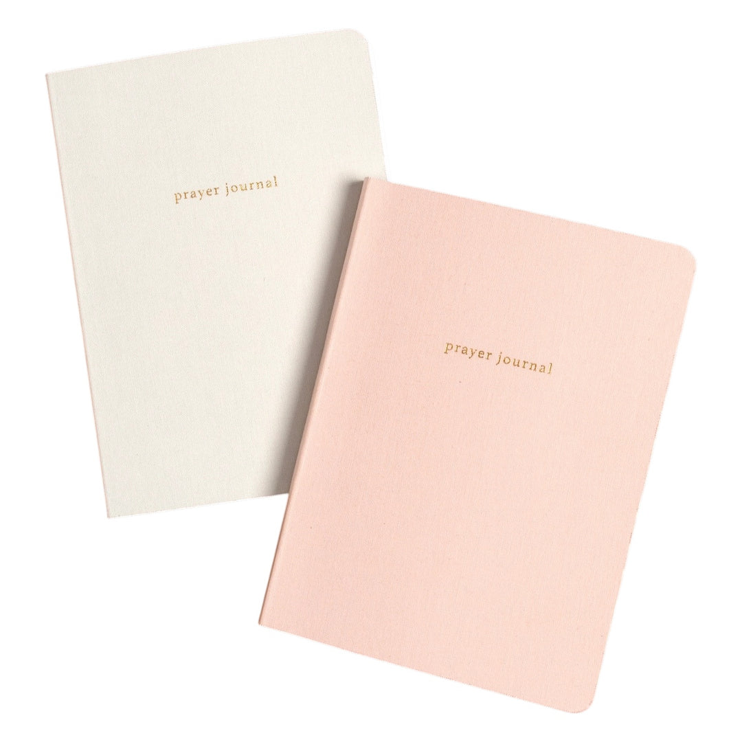 Two small prayer journals with rounded corners, one in cream and one in blush pink, both with &
